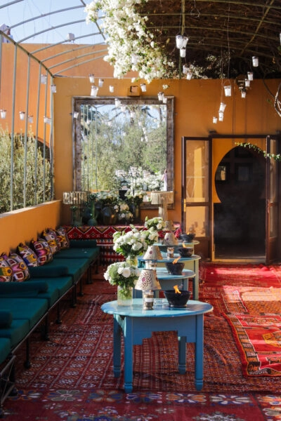 Colourful covered seating area with patterned rugs, turquoise tables and hanging flowers