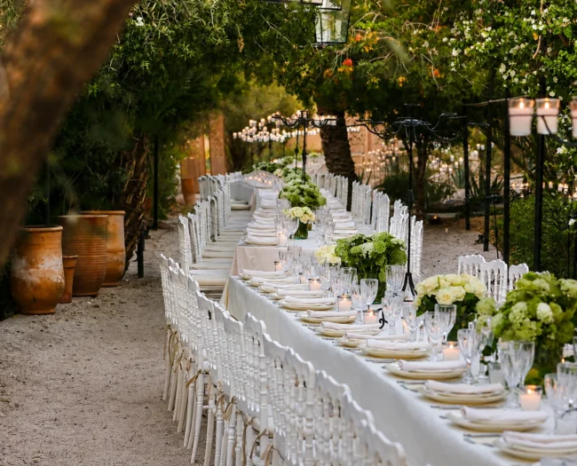 A long banqueting table with flowers and candles set under palm trees