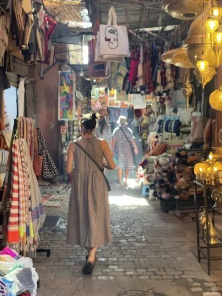TExploring a narrow Marrakech souk lined with textiles, bags and brassware
