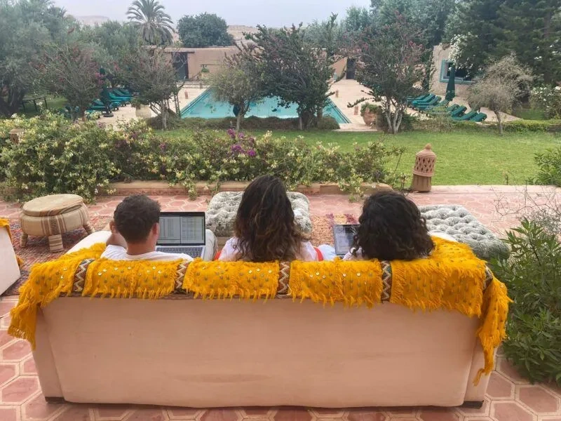 Sauveur team working on laptops on a terrace overlooking a garden and pool