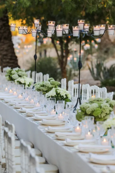 Long outdoor dining table with white flowers, taper candles and tall candelabra.