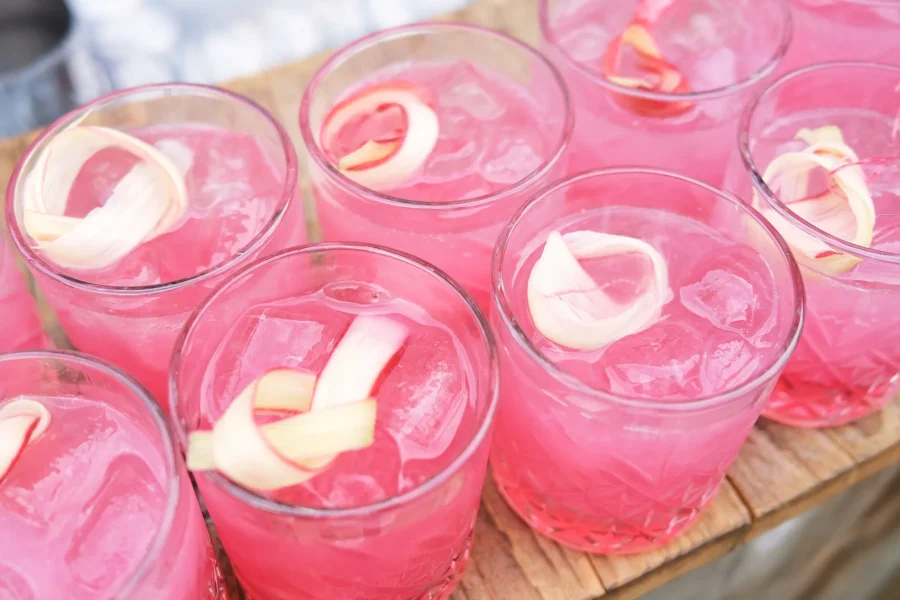 Pink drinks served over ice with curled garnishes on a wooden tray.