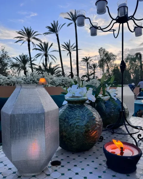 Lanterns, a lit candle and white lilies on a tiled terrace beneath palm trees.