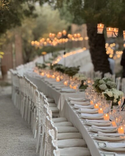 A long white table filled with candles positioned under palm trees in Morocco created by luxury event management from Sauveur Studios.